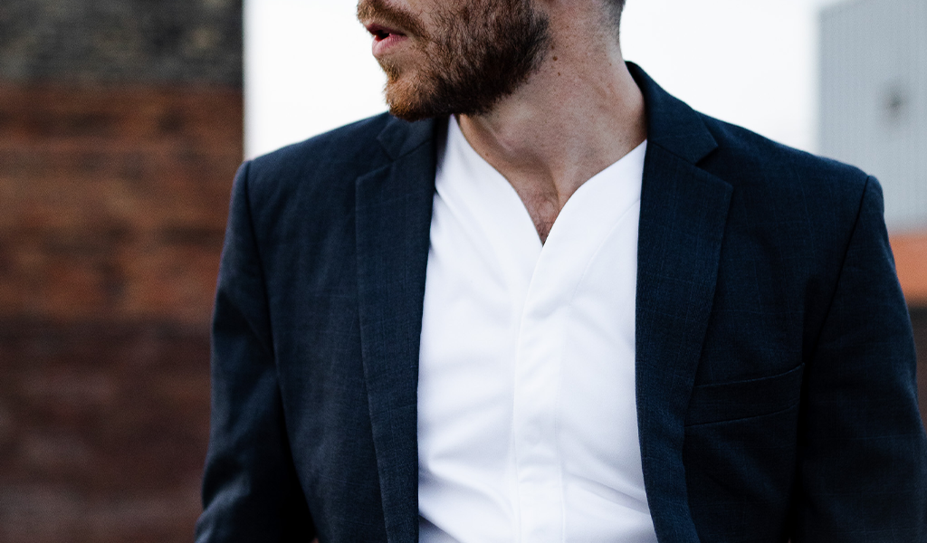 Close up of man wearing a white Cheegs collarless dress shirt with a suit jacket.