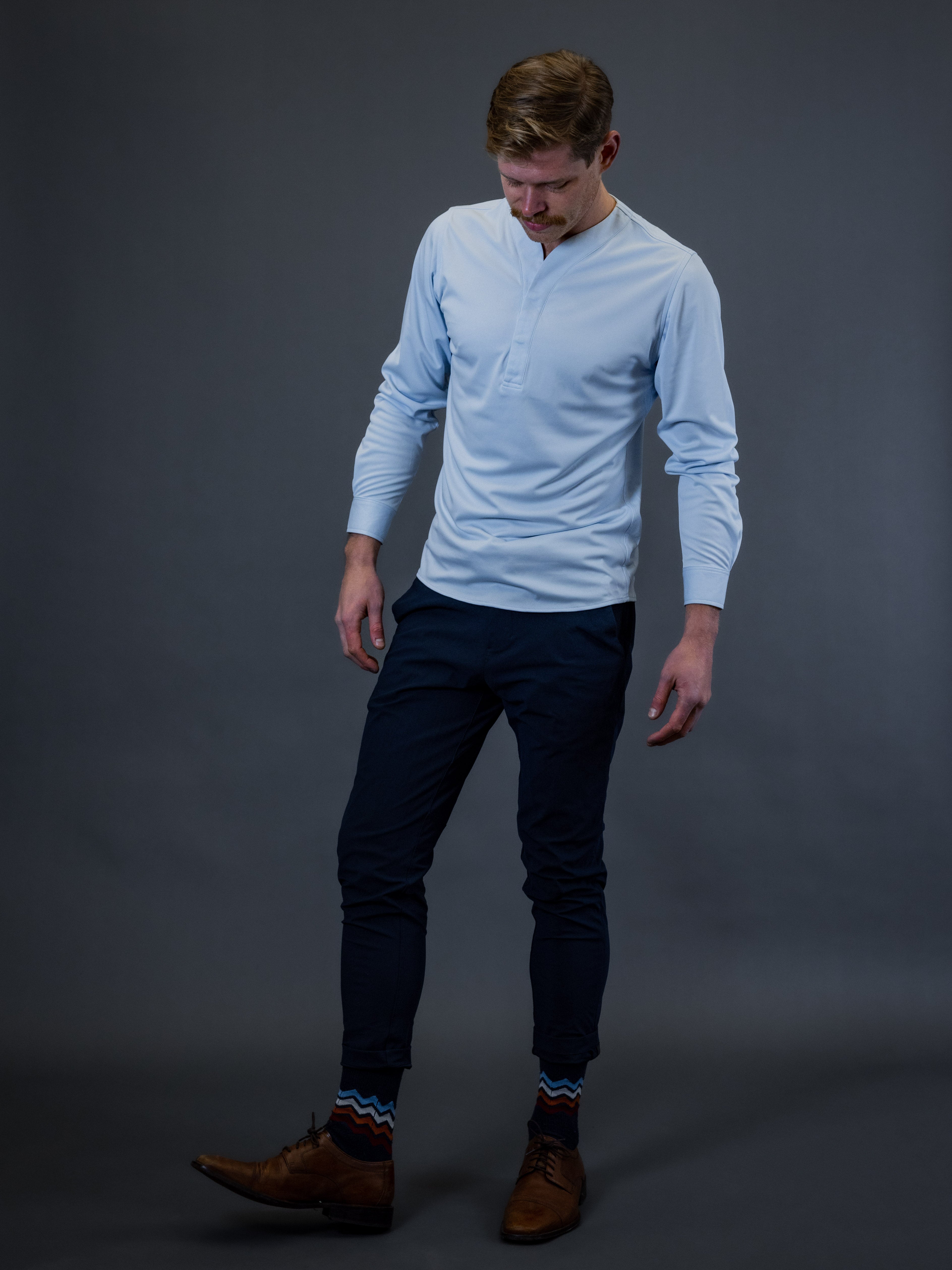 Male model wearing a light blue collarless dress shirt with long pants and dress shoes