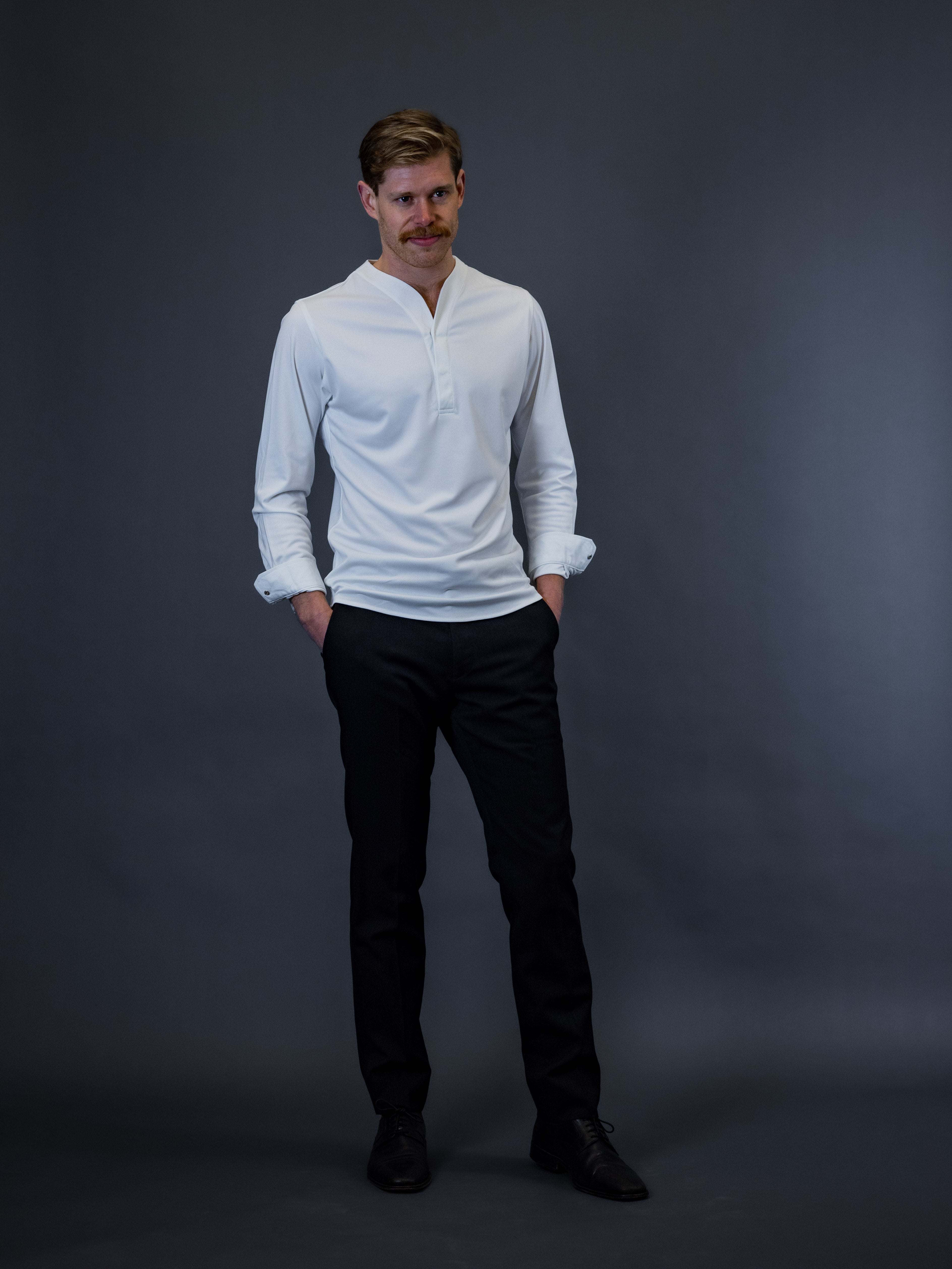 Man wearing dark pants and dress shows paired with a white collarless dress shirt