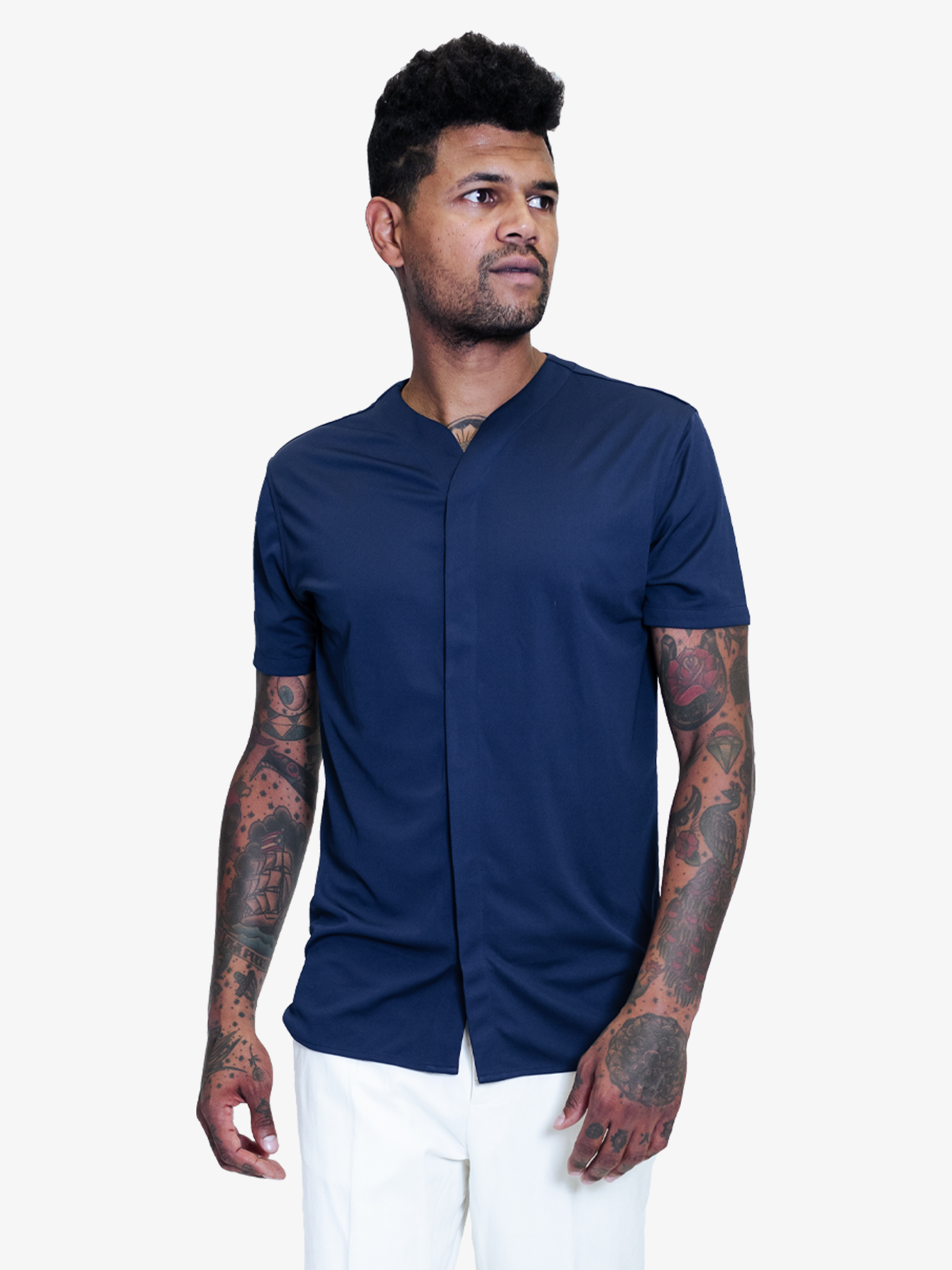 Man with tattoos wearing a dark blue collarless short sleeve shirt styled with white pants 