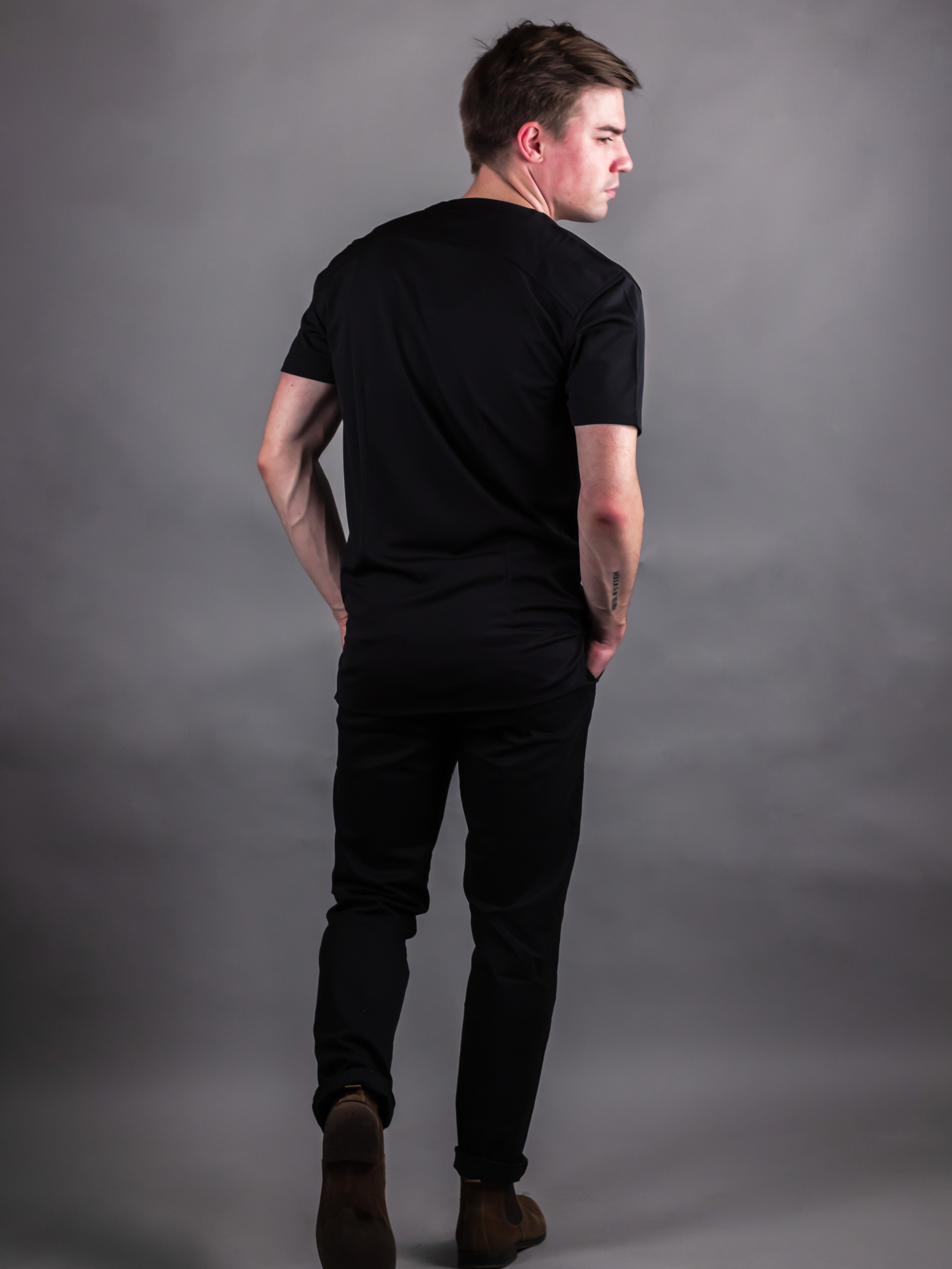 man showing the back of a mandarin collar short sleeve shirt in black styled with dark pants